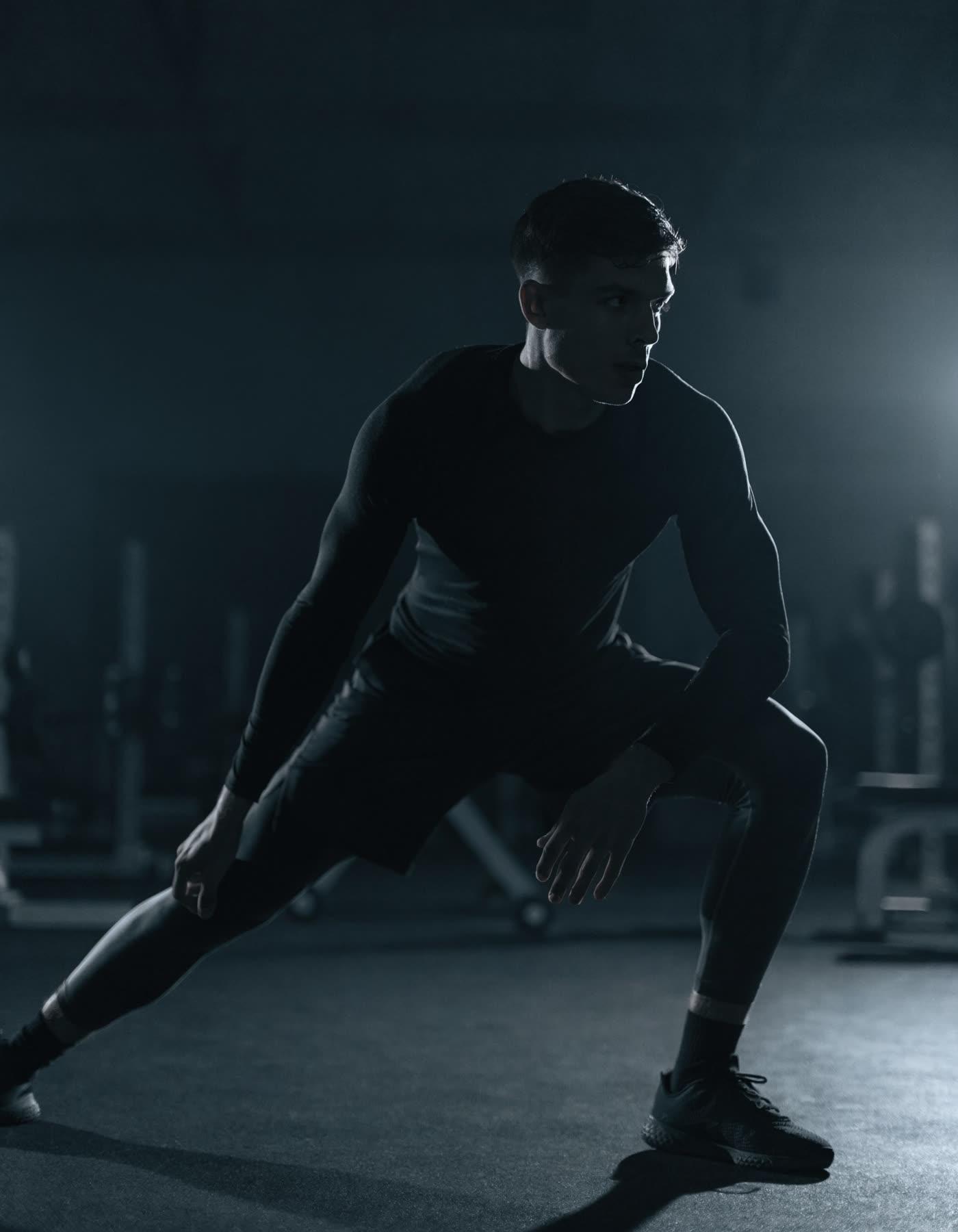 A trainer in a deep lateral lunge in a dark gym, an agility movement that mirrors pickleball court footwork.