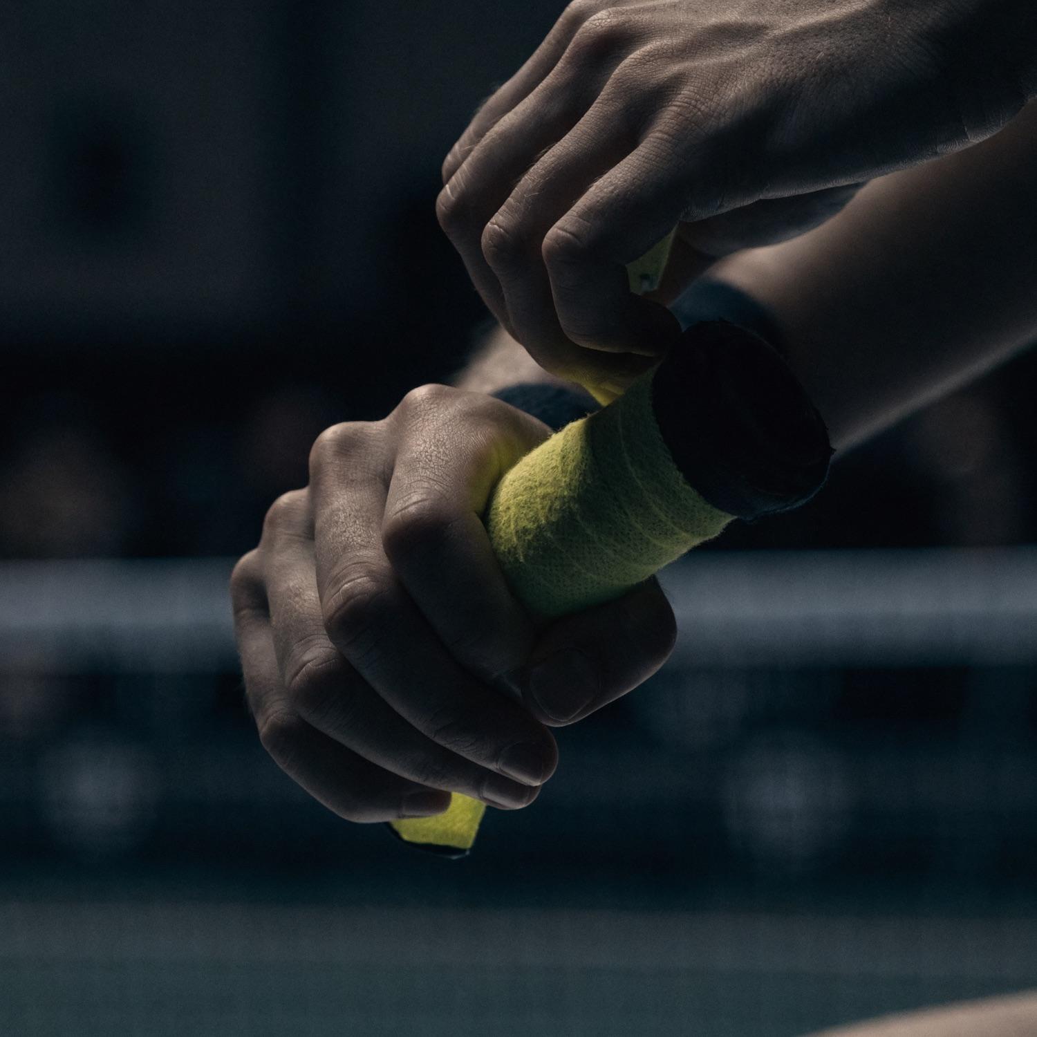 Close-up of a hand wrapping a cushioned paddle grip before a point. Representative detail image.