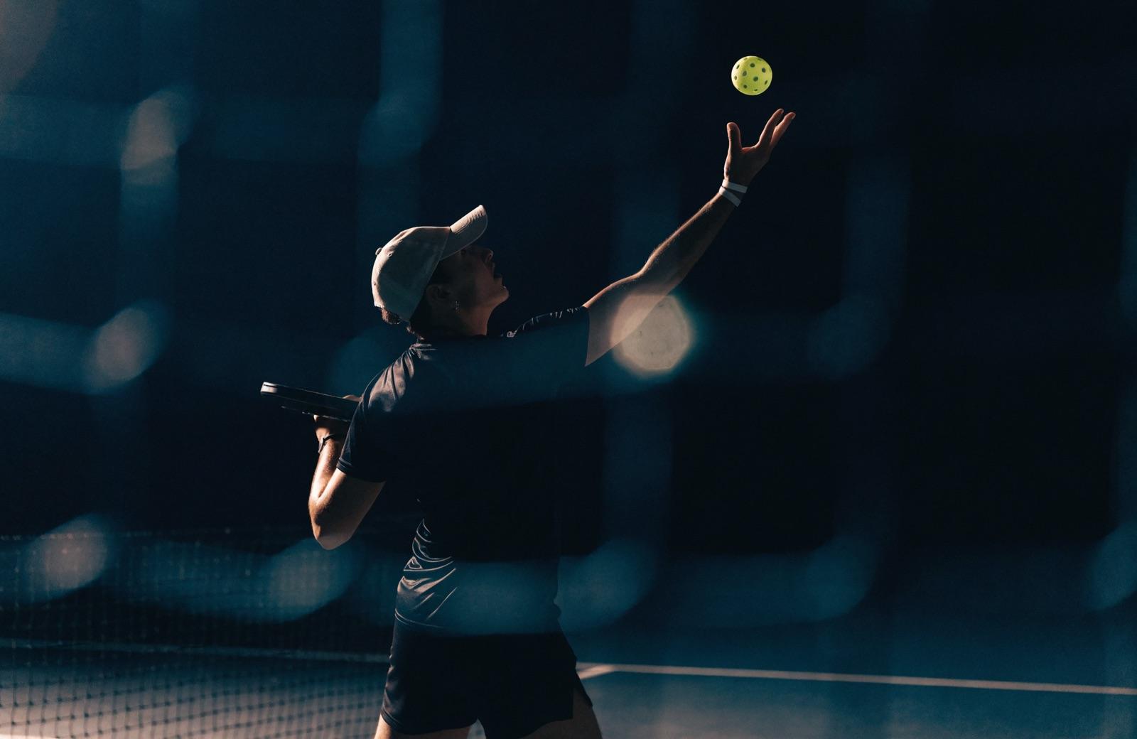 A player at the baseline tossing for a serve, paddle drawn back. Representative lifestyle image.